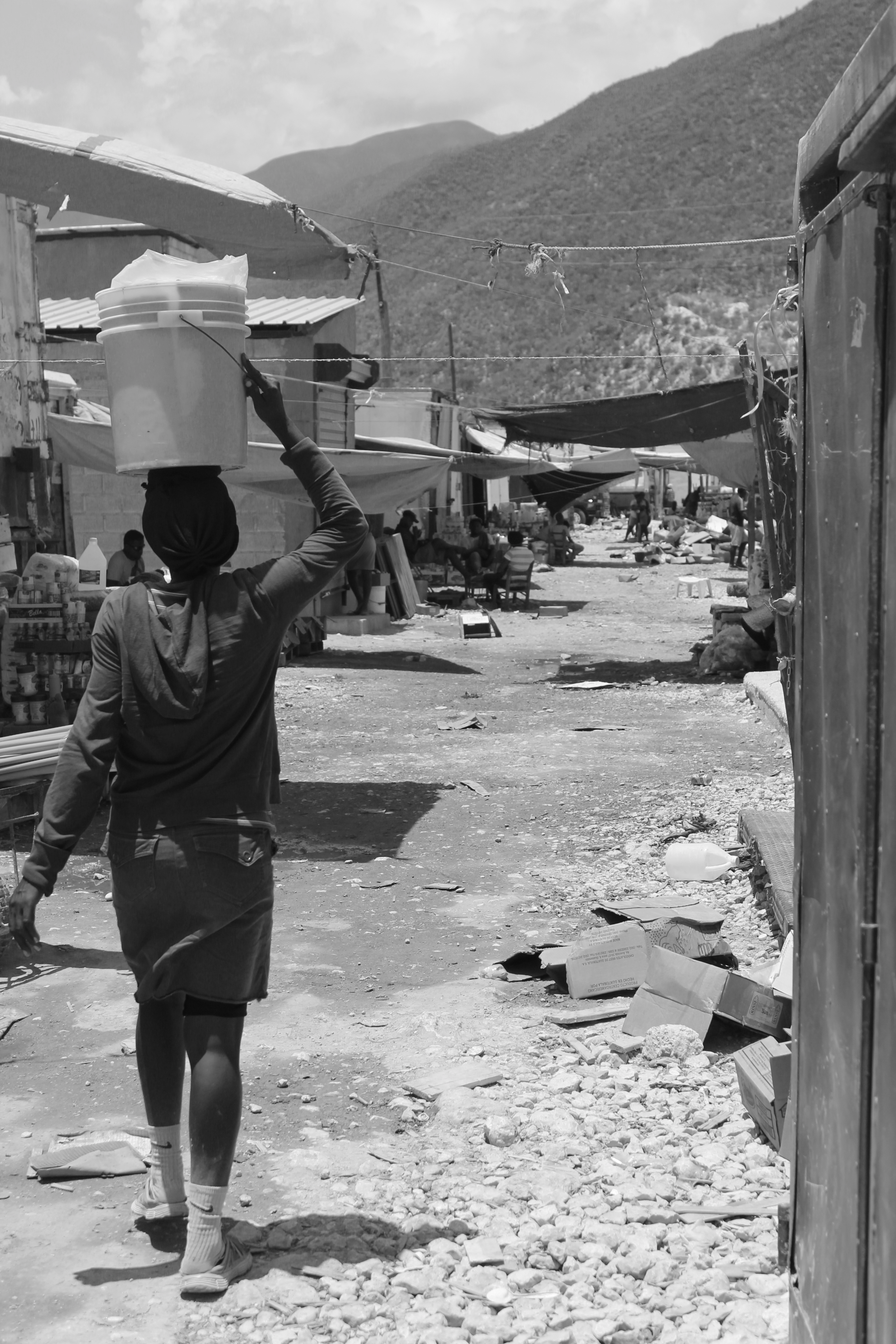 A woman carrying a bucket on her head filled with contents as she walks along the main road leading to the border crossing station.
