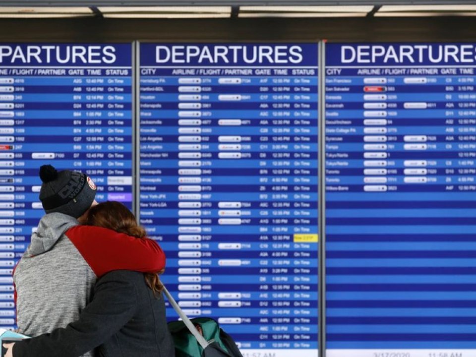 People embrace in front of a flight departures board at Dulles International Airport in Dulles, Va., March 17, 2020. At least 15 VOA journalists are to return to their country of origin in coming weeks, after USAGM did not renew their J-1 visas.