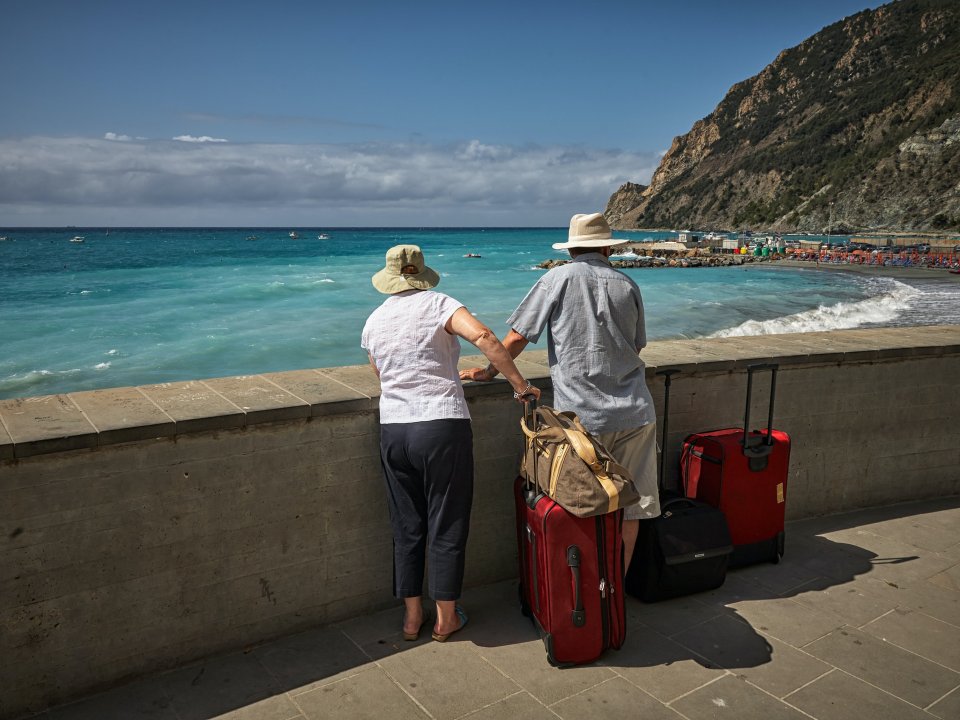Two tourists hold suitcases next to tropical beach