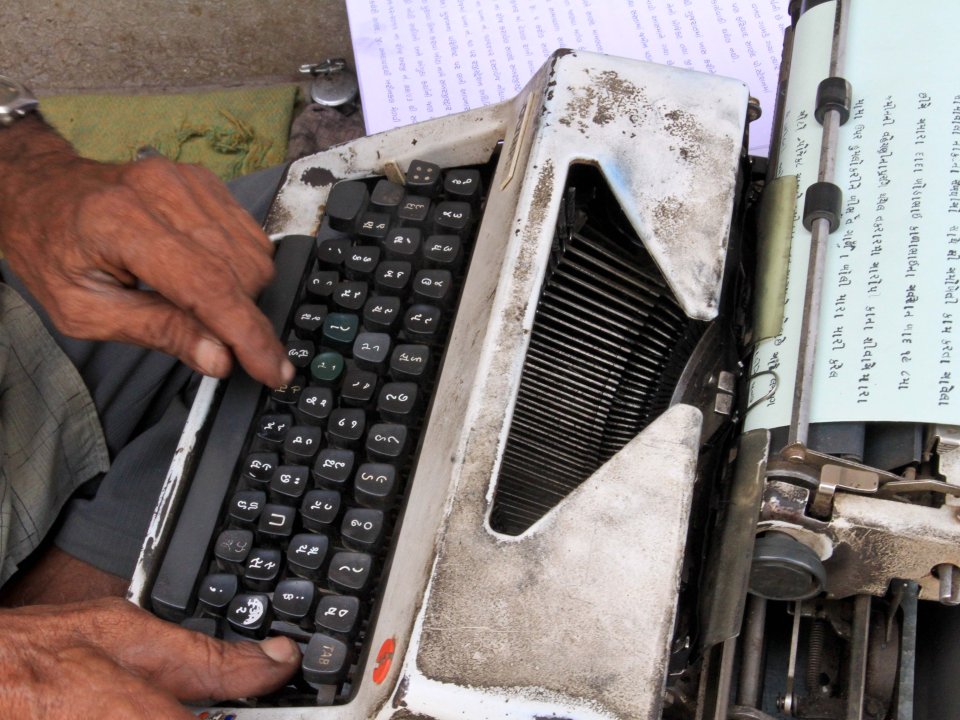 An Indian man's hands type on a typewriter.