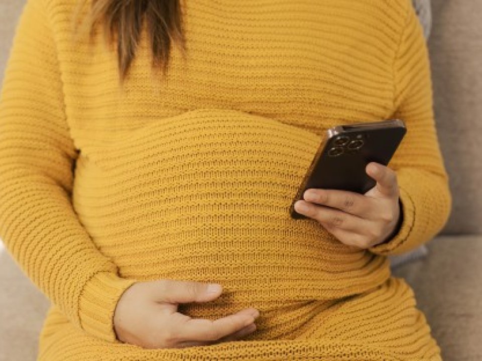 A pregnant woman sits in a chair while scrolling on a phone.