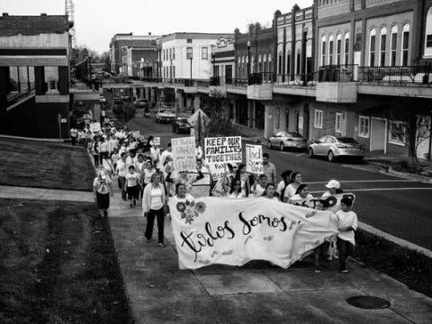 Protesters, dressed in white, walk down a street with a banner and signs.