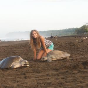 Undergraduate scholar squats next to sea turtles on a beach